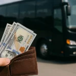 Hand holding wallet with cash in front of a black charter bus.